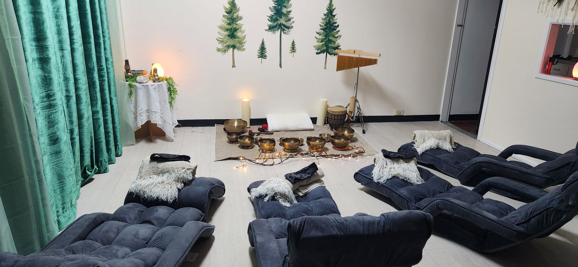 The full Hummingbowl Healing studio setup with blue velvet loungers, tree wall decals, candles and Tibetan singing bowls arranged on mats